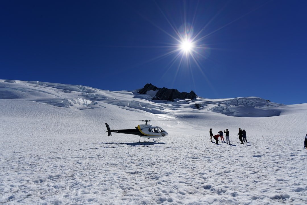 A helicopter trip to the Fox Glacier in New Zealand.  Image on the glacier with helecopter and people with backlit sun on the glacier. | Franz Josef in New Zealand