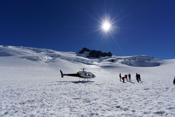A helicopter trip to the Fox Glacier in New Zealand.  Image on the glacier with helecopter and people with backlit sun on the glacier. | Franz Josef in New Zealand